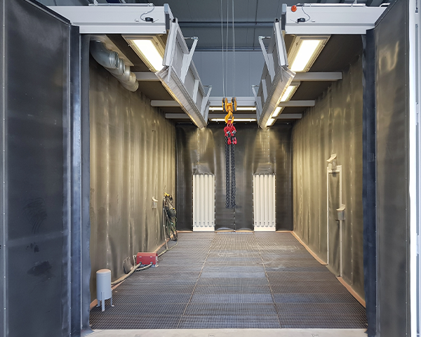 Innenansicht eines Sandstrahlhauses mit Beleuchtung, Gitterrostboden und Kranhaken